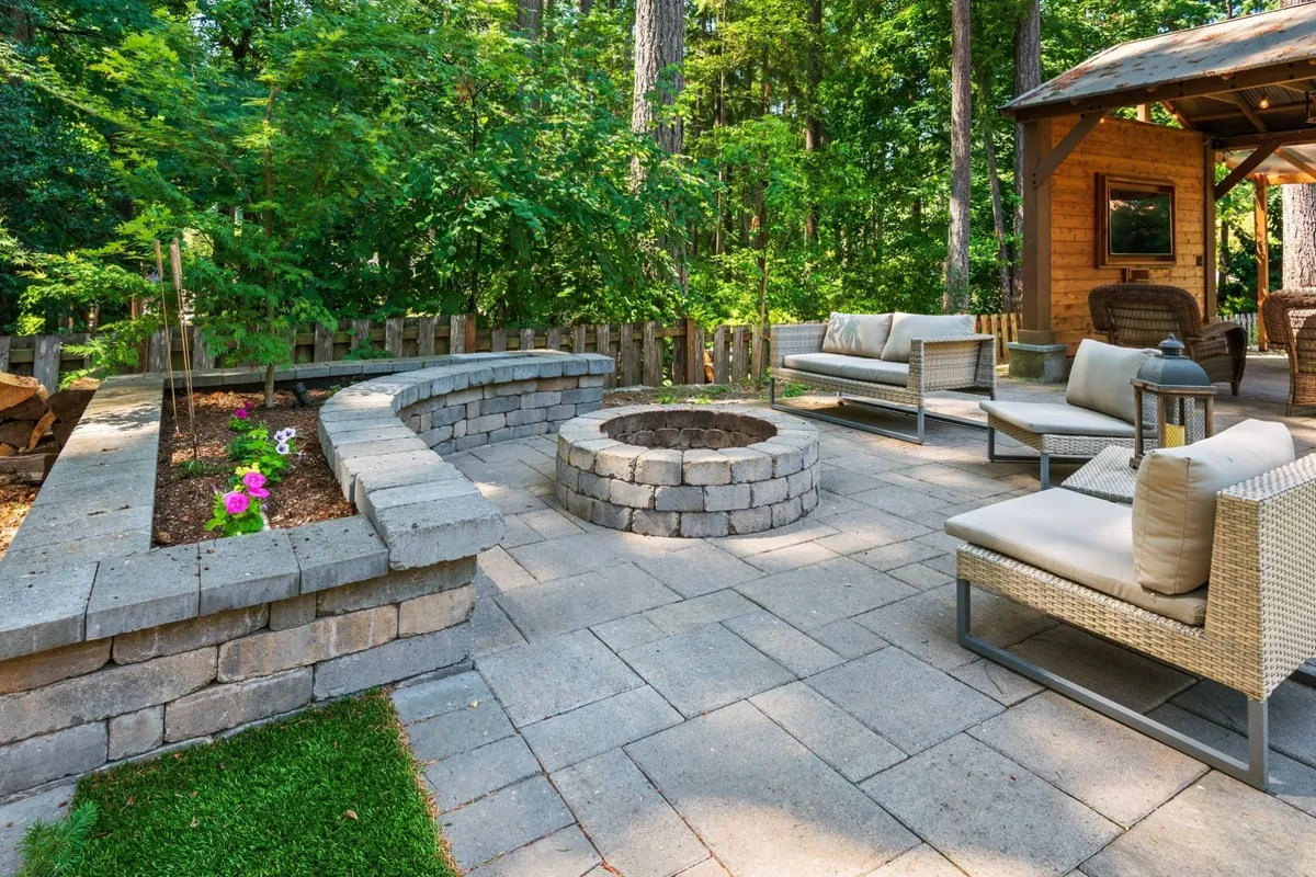 A cozy exterior evening scene featuring a fire pit encircled by comfortable seating and a vibrant flower bed, ideal for socializing, storytelling, and marshmallow toasting under the stars.