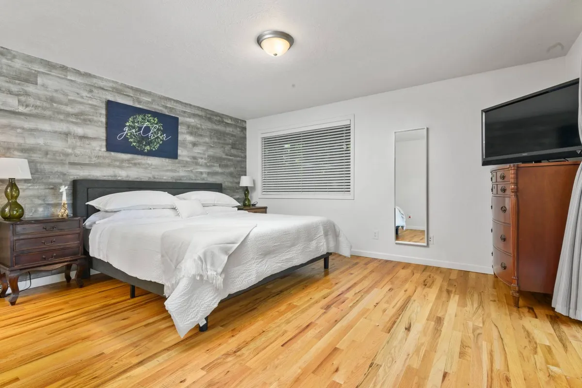 This image presents a restful bedroom with a contemporary bed, wooden flooring, decorative wall art, a wall-mounted mirror, and a television. The soft lighting and neutral tones create a relaxing and comfortable ambiance, ideal for unwinding after an active day.