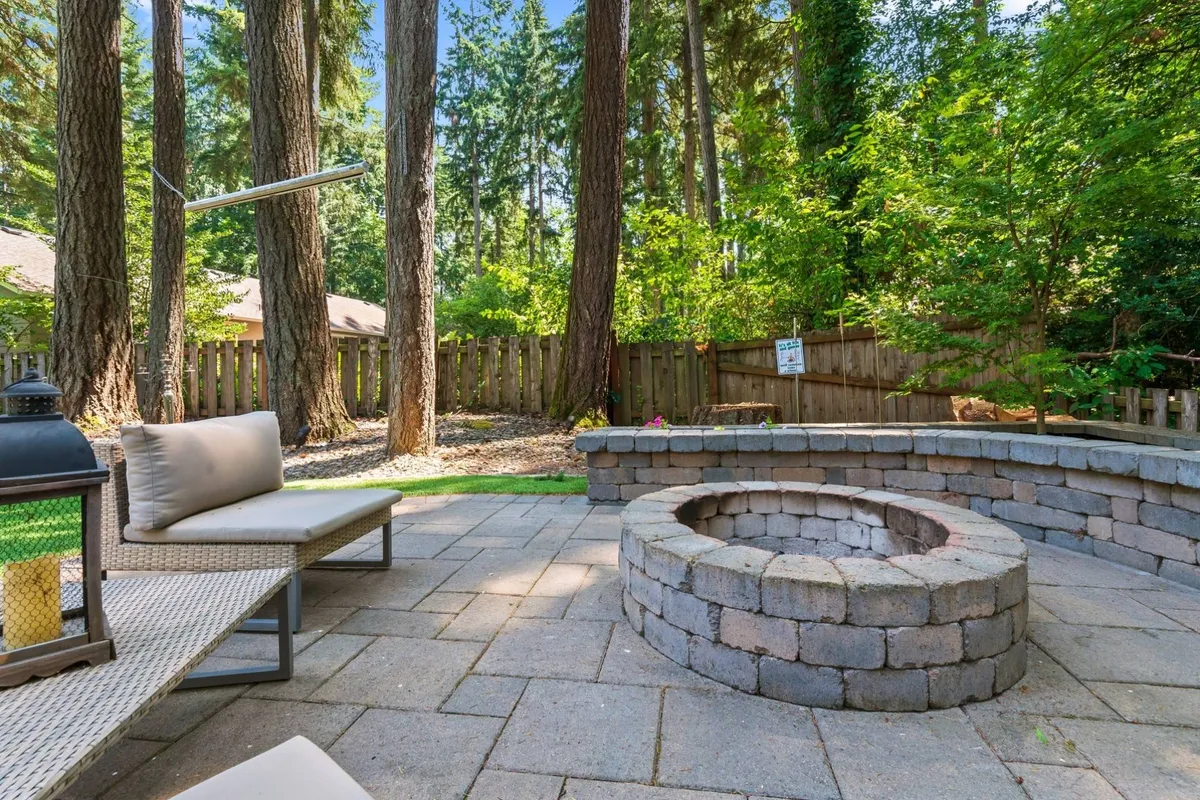 This exterior shot features a cozy fire pit area with comfortable seating surrounded by tall trees. The natural landscaping suggests ample space for walking, playing, and relaxing outdoors, making it appealing for pet owners seeking outdoor adventure and comfort for their furry companions.