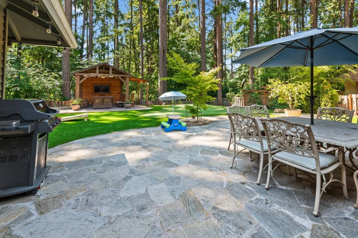 This image captures a lively backyard scene featuring an outdoor dining table, grill, gazebo, and a visible play area. The setup invites family gatherings, with ample space for both relaxation and children’s play. The colorful and cheerful mood signals fun and activity for all ages.