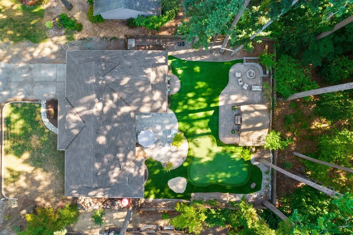 A serene backyard scene with a manicured lawn, a dedicated golf putting green, and a comfortable seating area shaded by mature trees. The patio is set up for morning coffee or sunset gatherings, and the overall landscape invites relaxation and golf practice in a private, peaceful setting.