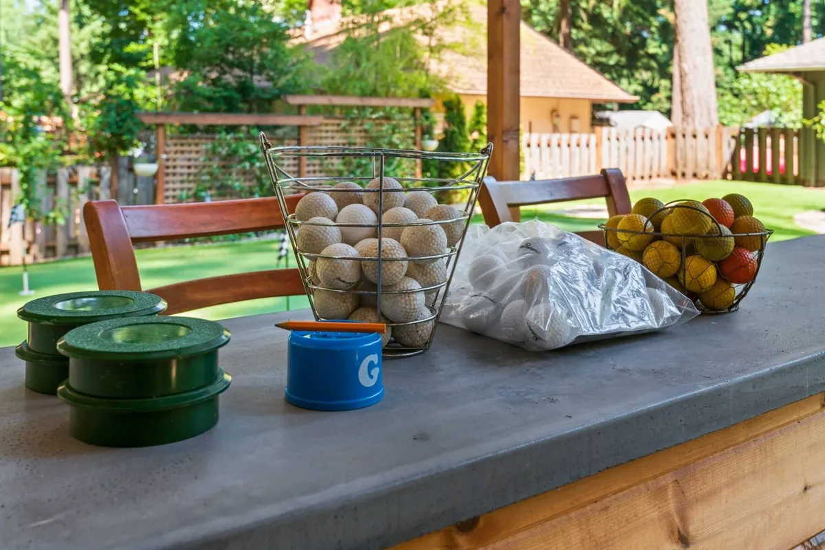 A playful arrangement of sports equipment, including a basket and bag filled with golf balls, a colorful assortment of tennis balls, and green storage containers. The casual vibe and variety of games suggest an area ready for friendly competitions and group fun.