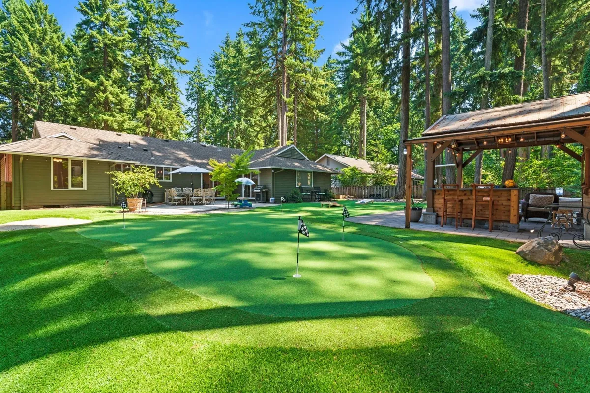 The image showcases the backyard of a single-family home at sunset, featuring a professionally landscaped putting green, a cozy outdoor seating area, and a charming gazebo. The space is designed for both relaxation and recreation, ideal for gatherings, casual golf games, and enjoying peaceful moments outdoors.