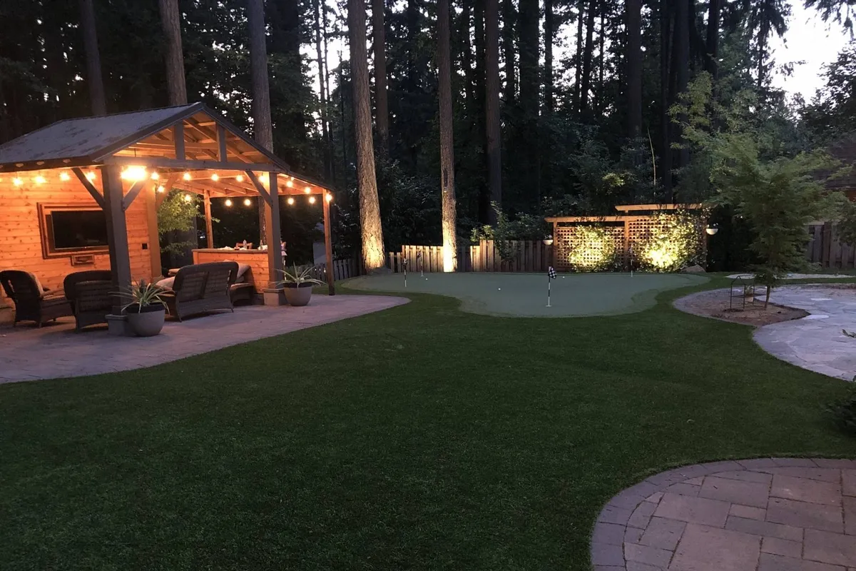 An inviting outdoor seating area beside a well-manicured putting green, enhanced by evening landscape lighting. The scene is set for a friendly golf competition or fireside chat, surrounded by lush landscaping and comfortable seating. A fire pit area is visible, ideal for recapping the day’s best shots or unwinding in the evening.